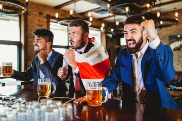 Men fans screaming and watching football on TV and drink beer in a pub