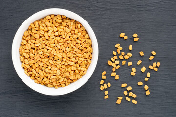 Fenugreek (Trigonella foenum-graecum) in ceramic bowl and bunch on black wooden background. Macro. Flat lay. Vegetarian food concept