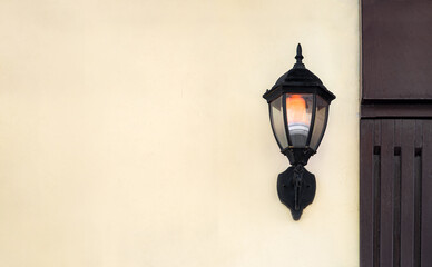 Fototapeta na wymiar iron wall lantern in retro style in black color with a glass shade and electric light bulb glow with warm light, urban wall lighting on the facade surface of the building with copy space, nobody.