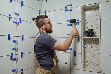 Tiler knocks the wedges of the ceramic tile leveling system off the wall in the bathroom