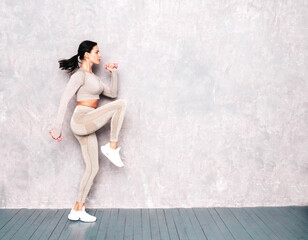 Fitness woman in sexy sports clothing. Young beautiful model with perfect body. Female posing in studio near grey wall at summer sunny day. Jumping and running. Doing exercises with dumbbells