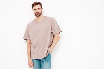 Portrait of handsome thoughtful stylish hipster lambersexual model. Sexy man dressed in pink T-shirt and jeans. Fashion male isolated on white wall in studio