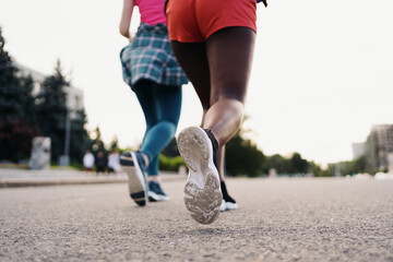 Back view of friends legs in sportswear running in the city. Multiethnic women having a fitness workout.