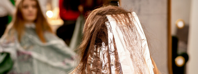 Beautiful young caucasian woman with foil in her hair while dyeing her hair sitting in a beauty...