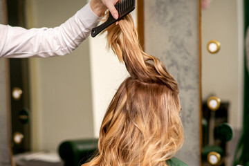 Naklejka premium Professional hair care. Young female blonde with long hair receiving hairstyling in a beauty salon