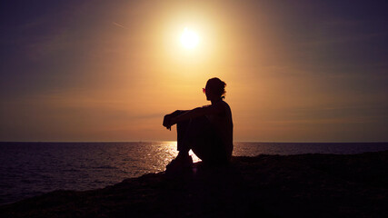 Obraz premium Silhouette of a woman watching sunset over distant horizon.
