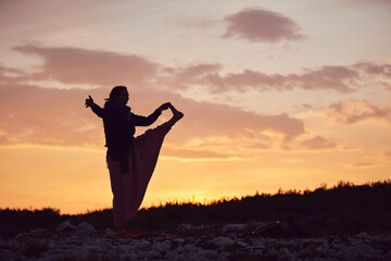 Fototapeta premium Woman practicing yoga outdoors in sunset sunrise time.