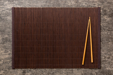 Two chopsticks and bamboo mat on cement background. Top view, copy space