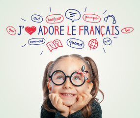Beautiful cute little girl with eyeglasses looking at I Love French text and illustrations. English: I Love French. Foreign language learning concept.