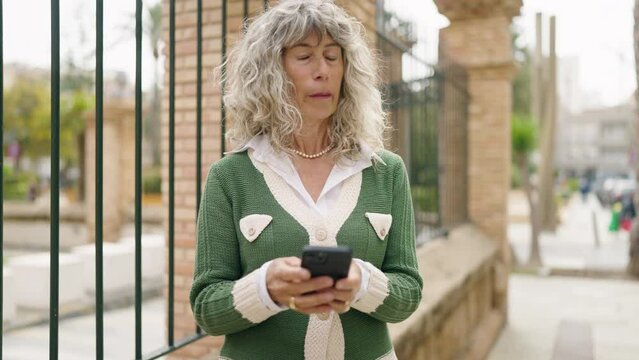 Middle age woman smiling confident using smartphone at street