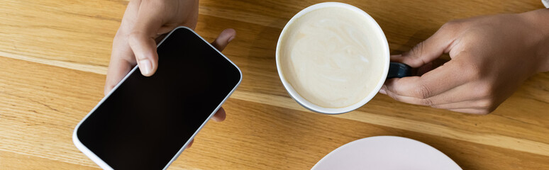 top view of african american man holding smartphone and cup of cappuccino, banner.