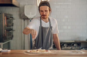 Man worker in a pizza place placing ingredients on pizza dough
