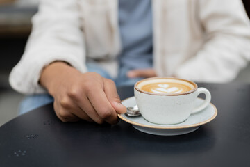 cropped view of african american man holding saucer with cup of cappuccino on summer terrace.