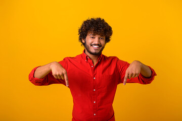 Here and now. Bearded handsome man pointing finger down, looking at camera with happy facial expression. Indoor studio shot isolated on orange background