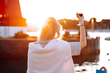 Rearview of woman holding elegant red wineglass on vacation in travelling. Cheers with dawn....