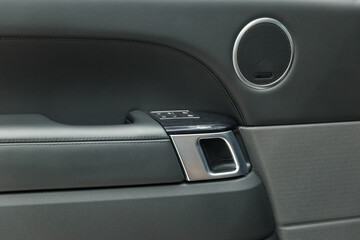 The concept of detailing. Black leather car door panel. Chrome door handle. The interior of the car. Interior trim of the car door, speaker, door lock control unit and door handle. Close-up.