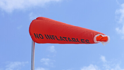 RNLI Flag and Orange windsock and Beach Warning Flags indicating sea hazard on sandy beach in UK