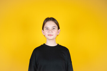 Teen girl in black clothes over yellow background. Portrait of a teenage girl without makeup