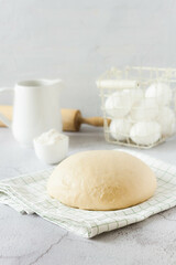 A ball of dough on a white rustic table with flour and a napkin. Homemade dough for pizza or bread.