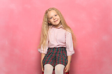 little girl schoolgirl sits in a chair. Pink background.