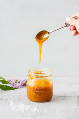 caramel sauce in a glass jar with a woman's hand and caramel dripping from a spoon on a light...