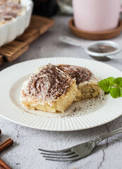 Sweet homemade buns with cream cheese and cinnamon on a white plate with mint decor from cinnamon sticks