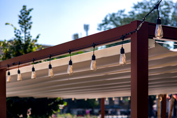 textile awning in the backyard wooden frame gazebo with a garland of strings of retro edison light...