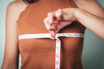 Slim woman measures her breast with a measuring tape - obrazy, fototapety, plakaty