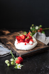 Dessert Pavlov with wild strawberries on a black background. Close-up of dessert with white cream and berries