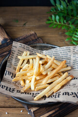 Delicious baked French fries close-up on an old newspaper in a metal plate on a wooden table