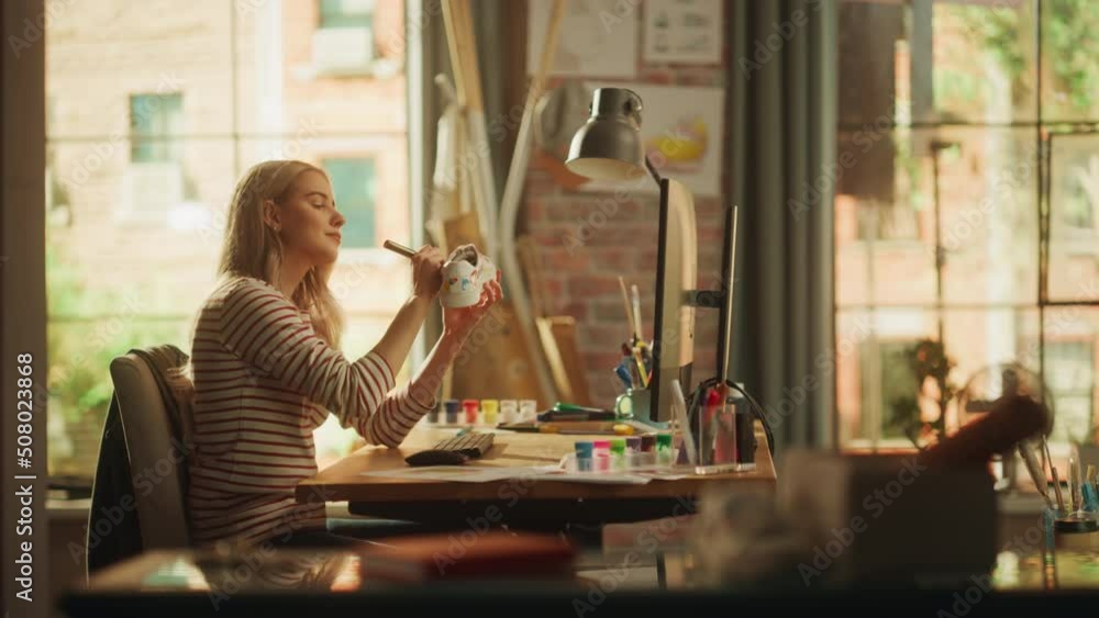 Poster side view of blonde female artist examining shoe while refreshing it in front of her laptop computer