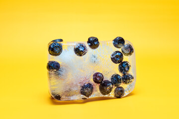 Blueberries in ice, yellow background. Stylish photo for computer desktops and mobile home screens.