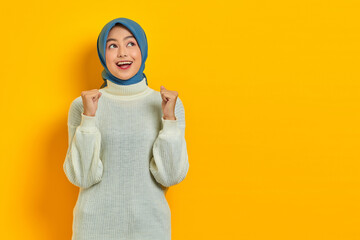 Excited beautiful Asian woman in white sweater celebrating big luck and success with raised fists...