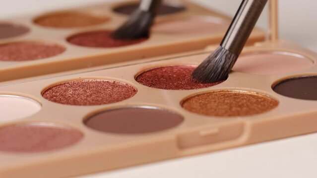 Make-up artist takes eyeshadows from cosmetic eyeshadow palette using brush.