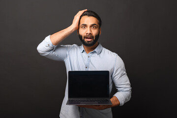 Discouraged Indian bearded freelancer guy holding and showing laptop computer with empty screen...