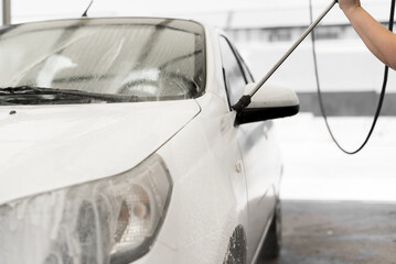 A woman's hand holds the hose lance to clean a white car under high pressure.