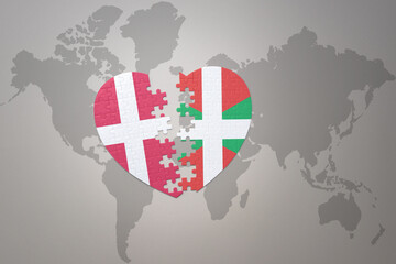 Fototapeta premium puzzle heart with the national flag of basque country and denmark on a world map background. Concept.