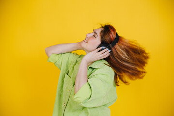 a red-haired beautiful woman stands on a yellow background in headphones listens to music and have fun and smiling