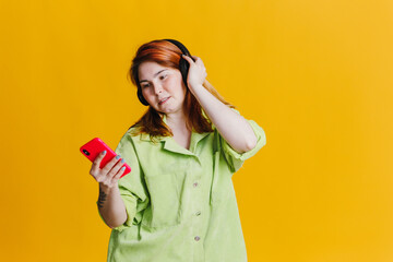 Red hair woman listening to music on her phone through headphones