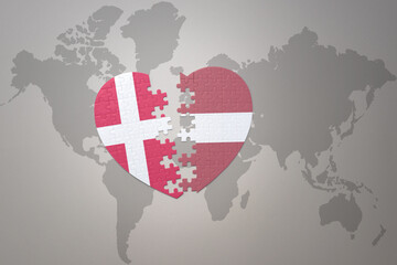 Fototapeta premium puzzle heart with the national flag of latvia and denmark on a world map background. Concept.