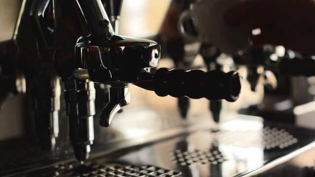Competent barista attaching portafilter to modern coffee machine for brewing hot aroma beverage. Fresh morning espresso coffee pouring into white ceramic cup.