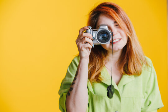 a red-haired beautiful woman stands on a yellow background with a photo camera and taking pictures