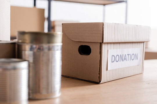Box with donation lettering near blurred canned food on table.