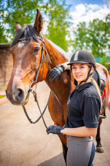 Lovely young woman wearing helmet stroking to her brown horse