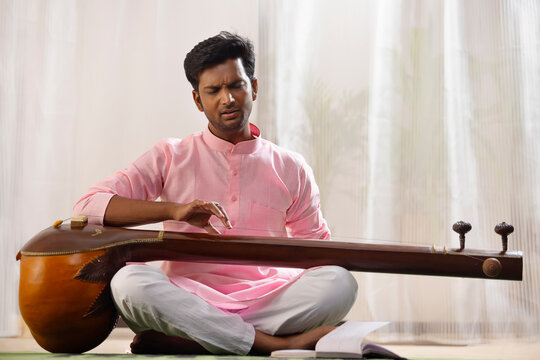 Young male classical singer playing Tanpura at home