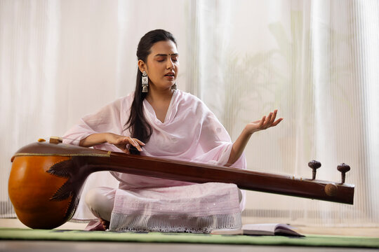 Young female classical singer playing Tanpura at home