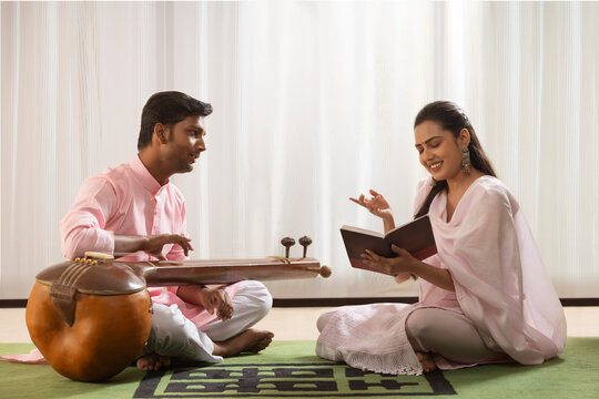 Young woman learning to play Tanpura with her music teacher at home