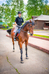 Lovely young woman wearing helmet riding her brown horse