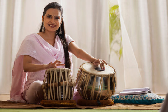Portrait of young woman playing Tabla at home