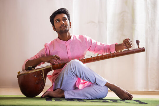 Young male musician tuning his sitar while sitting in living room